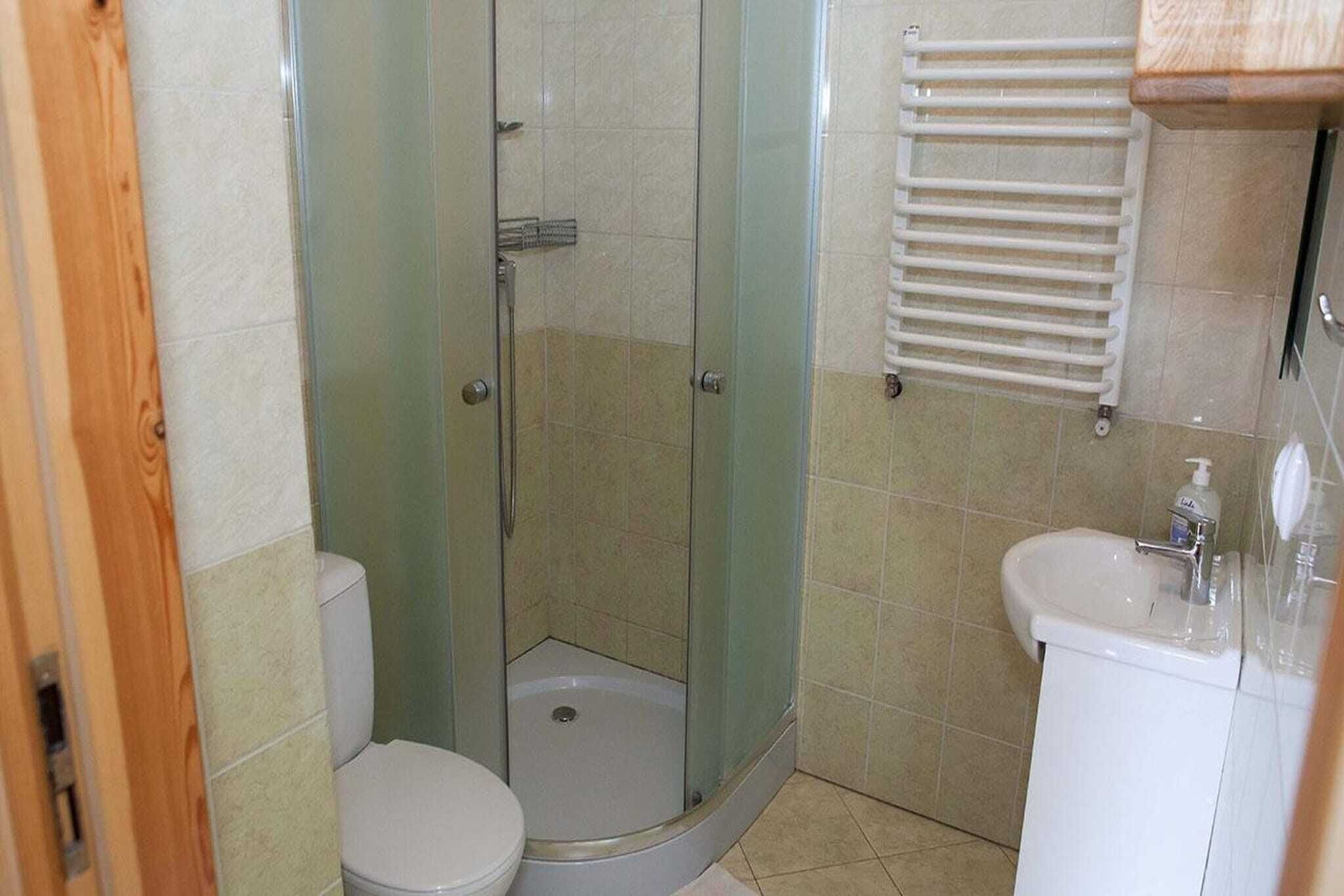 Een badkamer met een douche met glazen wand, een toilet en een wastafel met zeepdispenser.