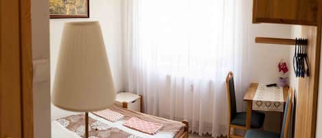 A bedroom with a bed, a desk, a chair, a lamp, and a window with curtains.