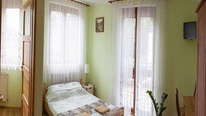 A room with a bed, a nightstand, a lamp, a painting, and a television on the wall.