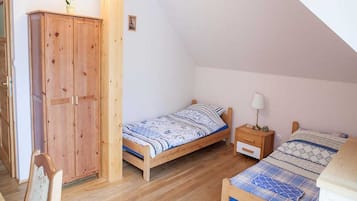 A bedroom with two wooden beds, a wooden wardrobe, and a small bedside table with a lamp.