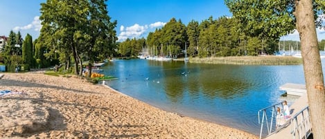 A sandy beach with a calm lake, boats, and trees.