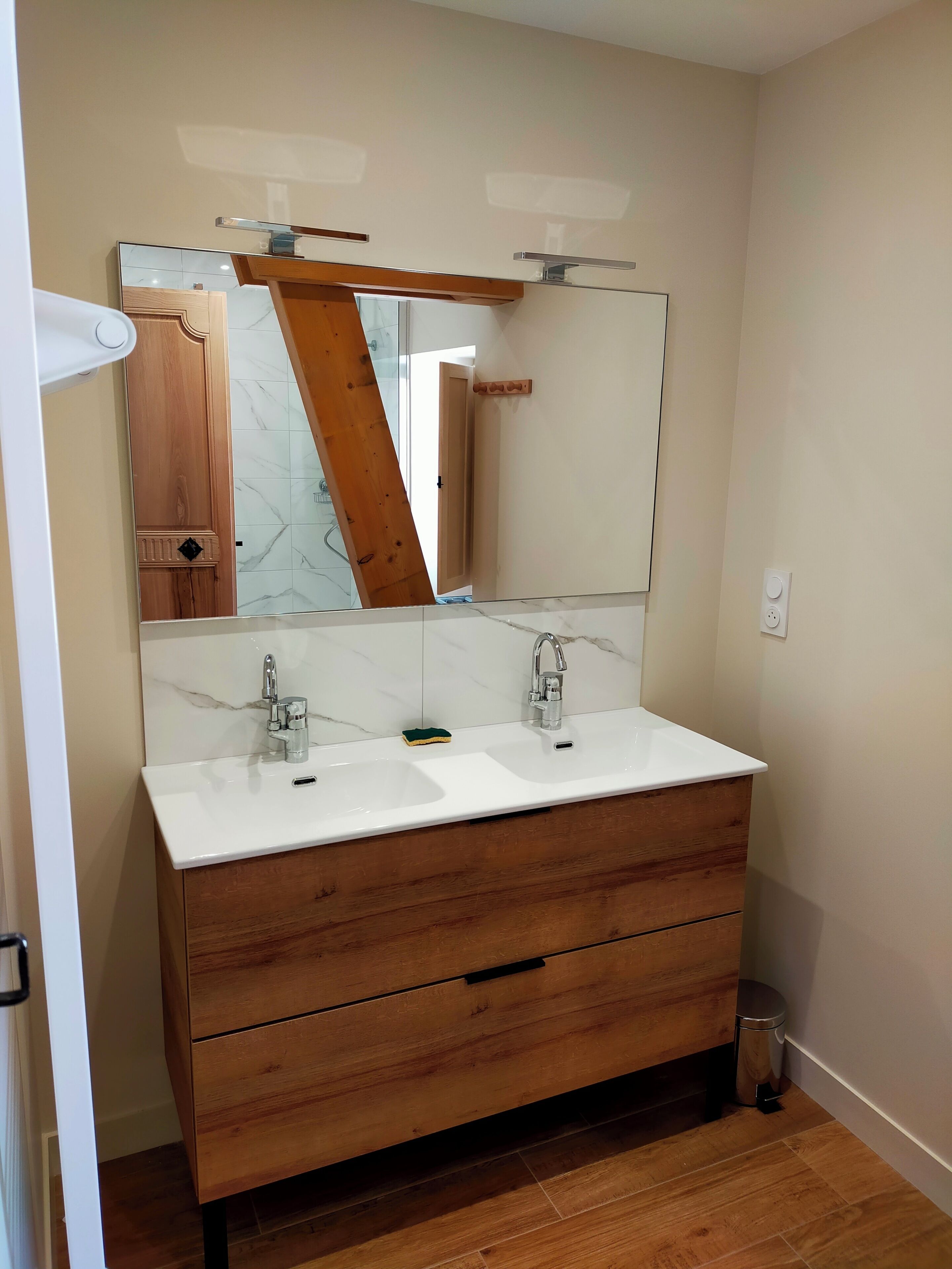 Une salle de bain avec un meuble-lavabo en bois, deux vasques, un miroir et un pare-feu en carrelage.