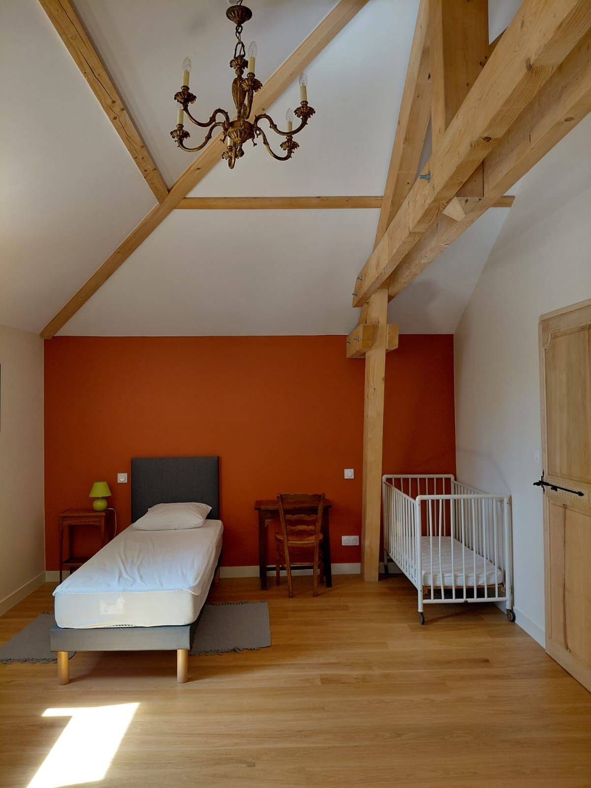 Une chambre à coucher avec un lit, une chaise, un berceau et un lustre.
