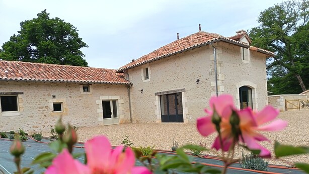 A building with a tiled roof and stone walls, a paved area in front, and a flower in the foreground. - Périgord. gite sleeps 8 or 12, 4*, private heated pool, large open spaces. (Lempzours)