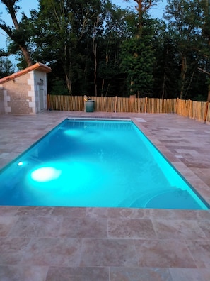 A rectangular swimming pool with a tiled deck, surrounded by a wooden fence and trees. - Périgord. gite sleeps 8 or 12, 4*, private heated pool, large open spaces. (Lempzours)