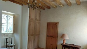 A room with a wooden ceiling, a chandelier, a large wooden door, a window, a table with a lamp, and a chair. - Périgord. gite sleeps 8 or 12, 4*, private heated pool, large open spaces. (Lempzours)