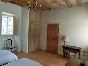 A room with a wooden ceiling, a chandelier, a large wooden door, a window, a table with a lamp, and a chair. - Périgord. gite sleeps 8 or 12, 4*, private heated pool, large open spaces. (Lempzours)