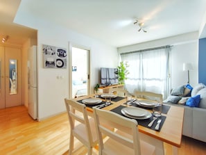 A dining area with a table set for four, a television, and a sofa with cushions. - Apartment 5 min. from the beach Palamós Costa Brava (Palamós)