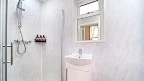 Ein Badezimmer mit Dusche, Waschbecken, Spiegel und Ablage für Toilettenartikel.