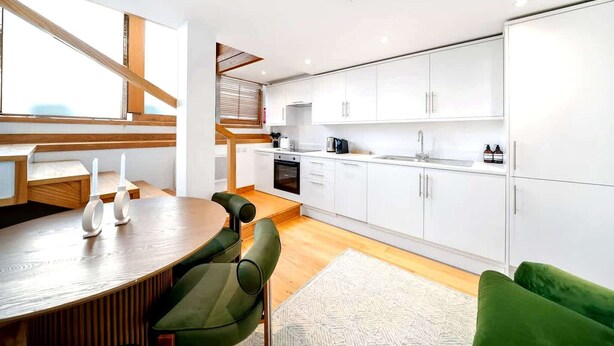 Een moderne keuken met witte kasten, een eethoek met een houten tafel en stoelen, en een trap met houten balken.