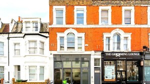 Een gebouw met een zwart etalage waarop 'The Grooming Lounge Fulham' staat, een fiets geparkeerd ervoor en het nummer '99' op het gebouw.
