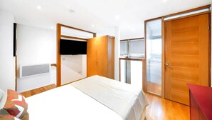 Een slaapkamer met een bed, een aan de muur bevestigde televisie, een kledingkast en een schuifdeur van glas.