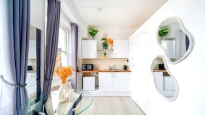 A modern kitchen with white cabinets, a microwave, and a sink. There is a glass table with a vase of flowers. - West Kensington Modern Couple Retreat (Greater London)
