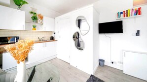 A modern kitchen with white cabinetry, a microwave, a sink, and a glass table. - West Kensington Modern Couple Retreat (Greater London)