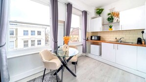 A modern kitchen with a dining area, large windows, and a view of buildings. - West Kensington Modern Couple Retreat (Greater London)