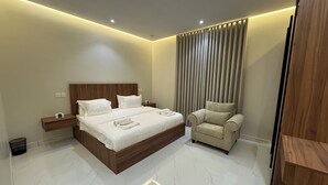 A modern bedroom with a large bed, bedside tables, a chair, and a curtain. - الشقق الفاخره luxury apartments (AL Madinah AL Munawwarah)