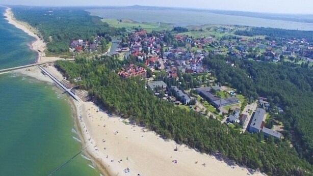 Vista aérea de uma cidade costeira com uma praia, uma ponte e edifícios residenciais.