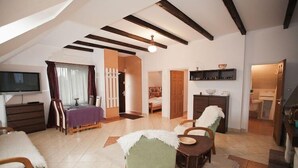 Uma sala de estar espaçosa com televisão, mesa de jantar e cadeiras. Escada leva a um andar superior.