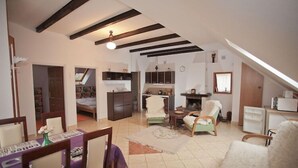 Quarto no sótão com teto inclinado, lareira, área de jantar com mesa e cadeiras, e cozinha com armários e geladeira.