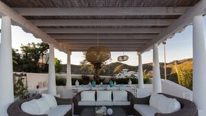 A covered outdoor seating area with wicker furniture and a table, overlooking a scenic landscape.