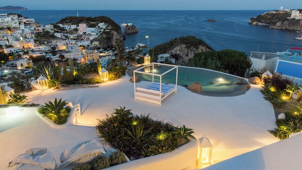 A resort with a pool, white buildings, and a view of the sea.