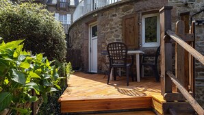 A stone building with a wooden deck, a table, and two chairs. - Studio Apartment 'Grand' with Sea View and Private Terrace (Perros-Guirec)