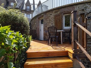 A stone building with a wooden deck, a table, and two chairs. - Studio Apartment 'Grand' with Sea View and Private Terrace (Perros-Guirec)