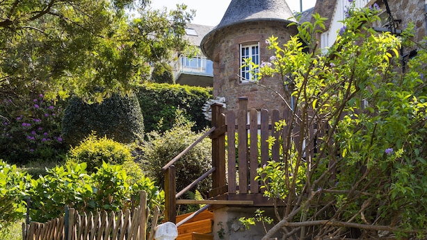 A stone tower with a conical roof, surrounded by lush greenery and a wooden fence. - Studio Apartment 'Grand' with Sea View and Private Terrace (Perros-Guirec)