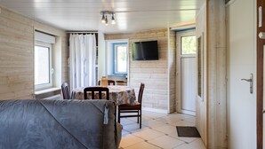 A room with a bed, a table with chairs, a TV mounted on the wall, and a window with curtains. - Studio Apartment 'Grand' with Sea View and Private Terrace (Perros-Guirec)