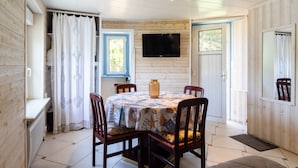A dining area with a table, chairs, a television, and a window with curtains. - Studio Apartment 'Grand' with Sea View and Private Terrace (Perros-Guirec)