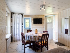 A dining area with a table, chairs, a television, and a window with curtains. - Studio Apartment 'Grand' with Sea View and Private Terrace (Perros-Guirec)