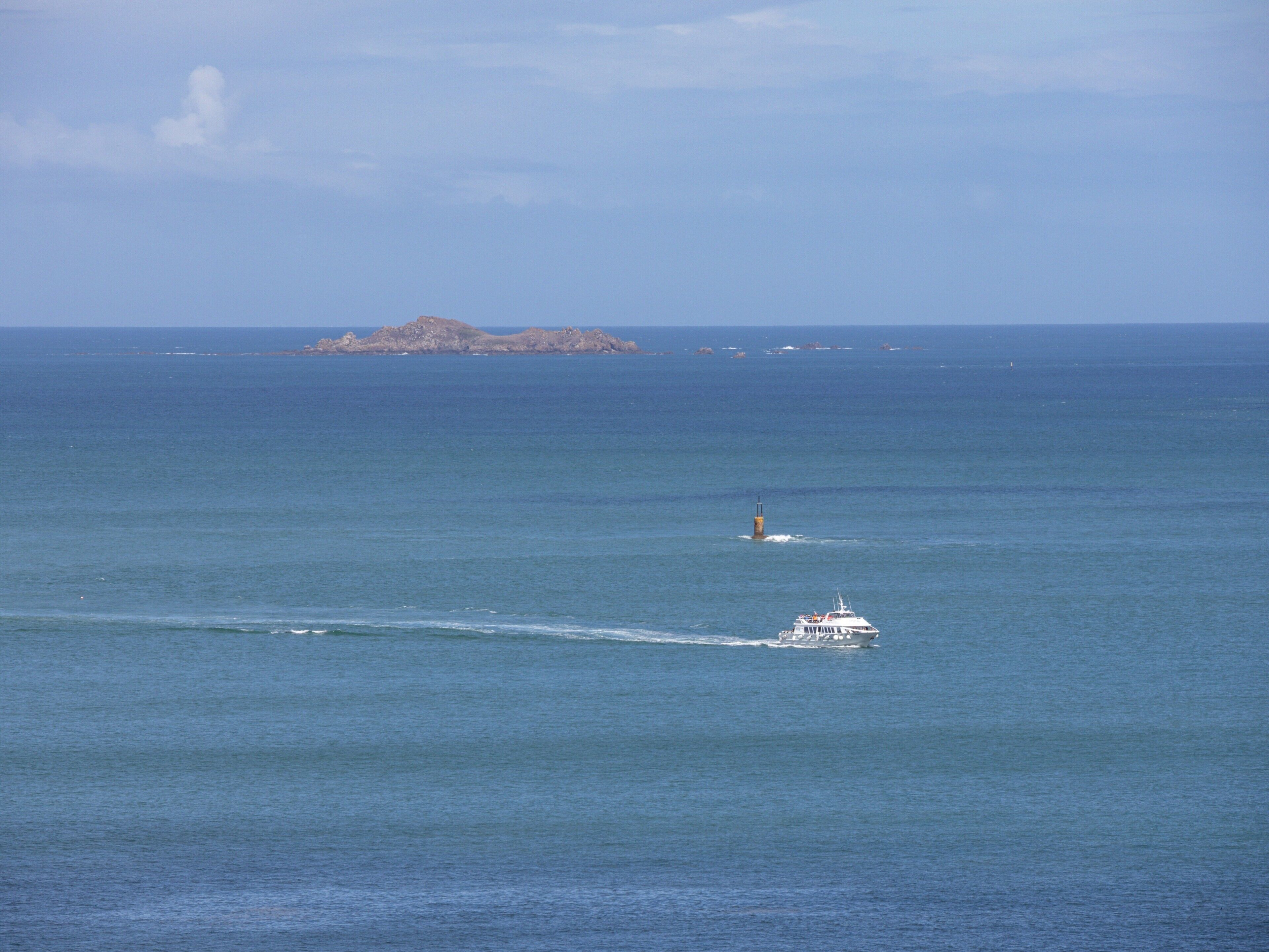 A boat moving across a calm sea with a distant island and a lighthouse.