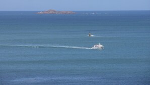 Ein Boot fährt über ruhiges Meer, im Hintergrund eine Insel und ein Leuchtturm.