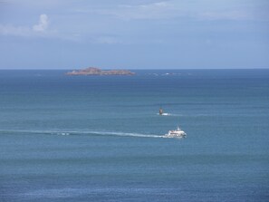 A boat moving across a calm sea with a distant island and a lighthouse. - Cote de granit rose, vue mer, studio ground floor renovated this year (Perros-Guirec)