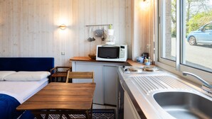 Eine kleine Küchenzeile mit Mikrowelle, Kaffeemaschine und Geschirr, ein kleiner Esstisch und ein Fenster mit Blick auf einen Wagen draußen.