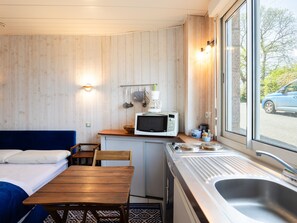 A compact kitchenette with a microwave, coffee maker, and utensils, a small dining table, and a window with a view of a car outside. - Cote de granit rose, vue mer, studio ground floor renovated this year (Perros-Guirec)