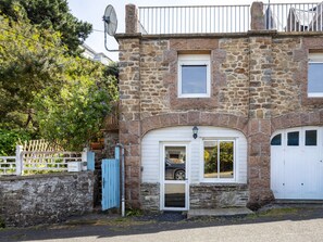 A stone building with a garage, a white door, and a satellite dish. - Cote de granit rose, vue mer, studio ground floor renovated this year (Perros-Guirec)