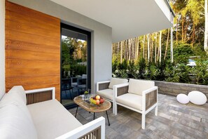 Ein moderner Außenbereich mit einer Holzwand, einer Glastür, die in einen Garten führt, und einem weißen Sofa für draußen.