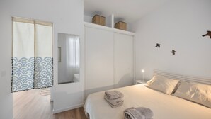 Un dormitorio con cama, armario, espejo y ventana con cortinas.