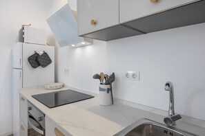Una cocina moderna con horno empotrado, estufa, pileta y encimera con hervidor y especias.