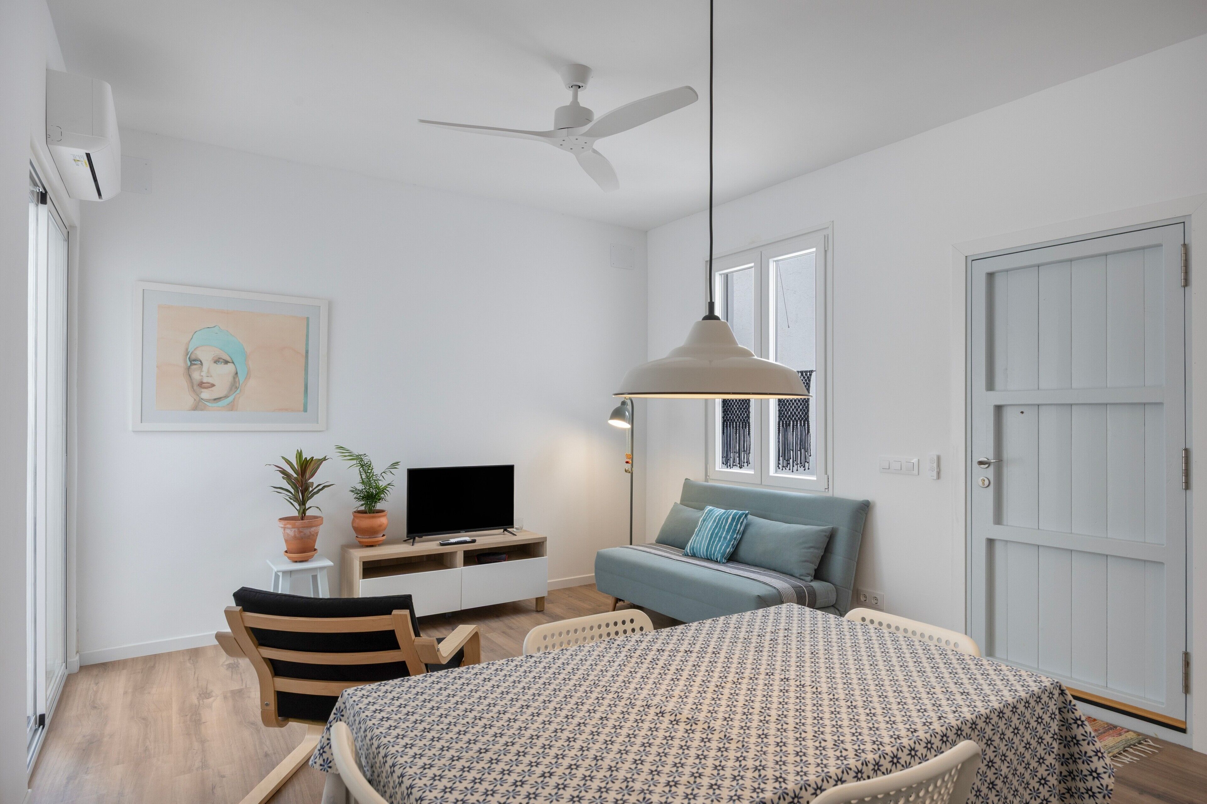A bedroom with a bed, a desk with a TV, a ceiling fan, and a window.