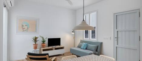 A bedroom with a bed, a desk with a TV, a ceiling fan, and a window.