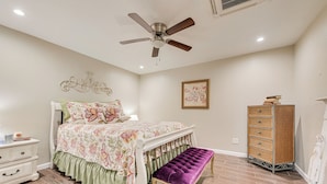 Ein Schlafzimmer mit einem Bett, einer Bank, einem Schminktisch, einem Deckenventilator und einem an der Wand hängenden Bild.