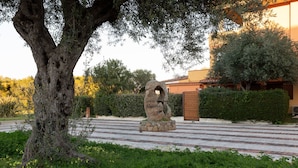 A stone sculpture in a landscaped area with a tree and a building in the background. - Alba Marina by Wonderful Italy (Olbia)