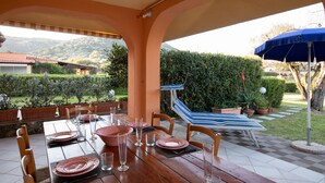 An outdoor dining area with a wooden table set for four, surrounded by chairs, and an umbrella providing shade. - Alba Marina by Wonderful Italy (Olbia)