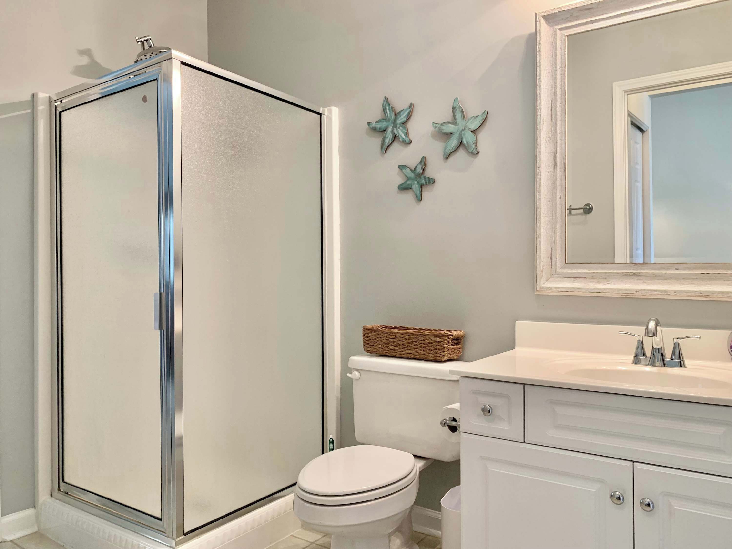 A bathroom with a glass-enclosed shower, a toilet, a vanity with a mirror, and decorative starfish on the wall.