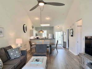 A living room with a sofa, a coffee table, a dining area with chairs, a kitchen with appliances, and a ceiling fan. - Peaceful 2Bed/2Bath Condo | King Bed | Pool View (North Myrtle Beach)