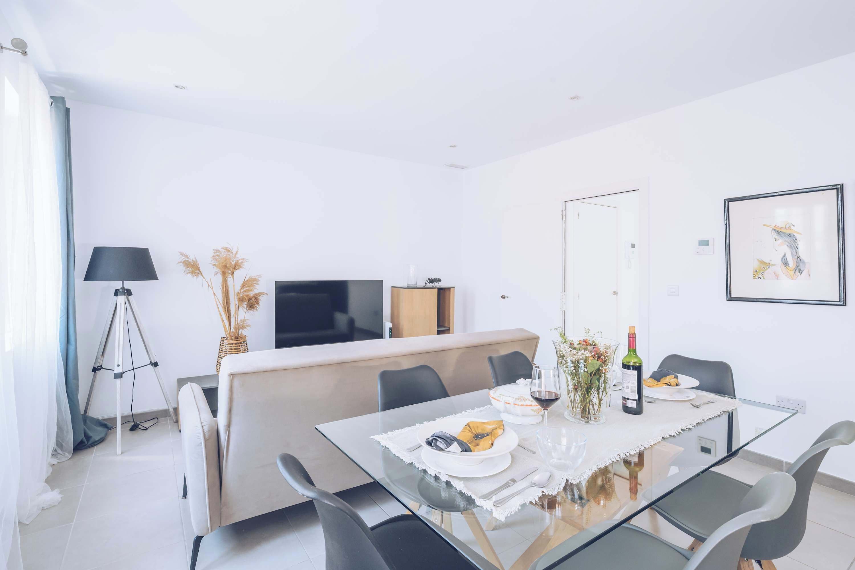 Un espace repas moderne avec une table en verre, des chaises noires, un canapé, un téléviseur et un tableau encadré au mur.