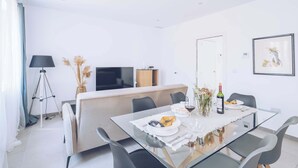 A modern dining area with a glass table, black chairs, a sofa, a TV, and a framed picture on the wall.