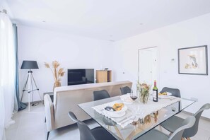 Ein moderner Essbereich mit einem Glastisch, schwarzen Stühlen, einer Couch, einem Fernseher und einem gerahmten Bild an der Wand.